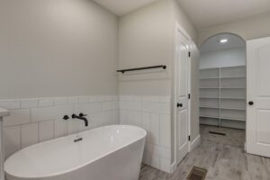 A bathroom with a tub, toilet and shelves.