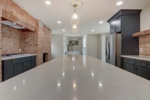 A large kitchen with white counters and brick walls.