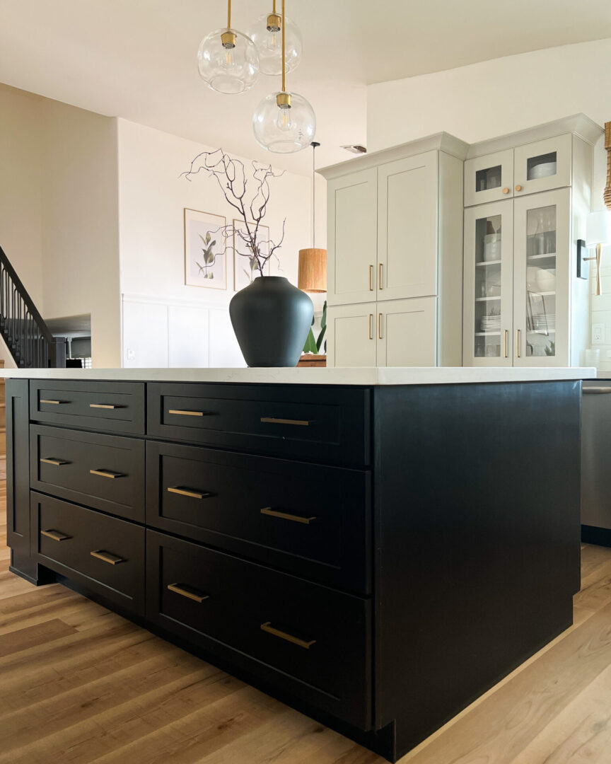 Builders Flooring & Design project gallery three toned kitchen cabinets, paint and wood door styles. Modern farmhouse kitchen cabinets in black and white paint and warm wood. White custom kitchen hood. Black center island with drawers and build in appliances.