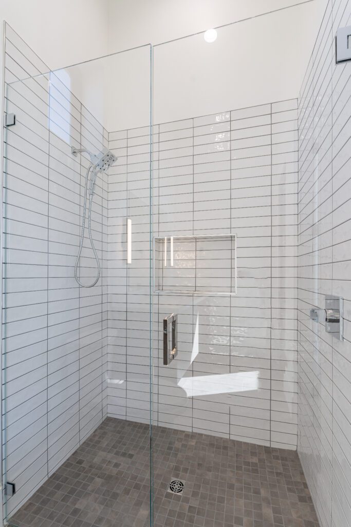 A bathroom with white tile and glass shower doors.

