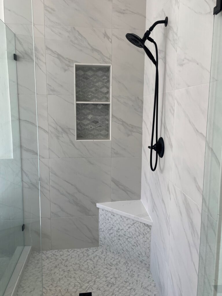 A bathroom with marble walls and floor, and a black shower head.

