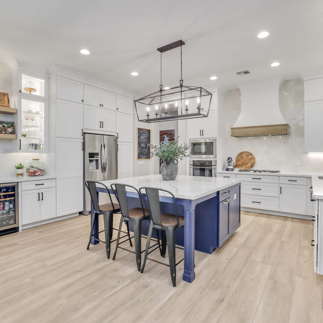 A kitchen with white cabinets and blue island.