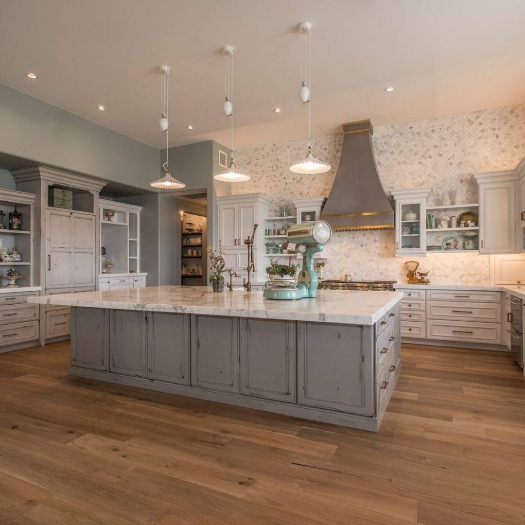 White distressed kitchen cabinets with large quartz countertop island and hardwood floors. Open kitchen shelving and decor.